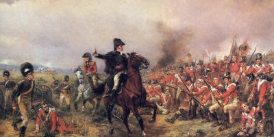 Wellington en Waterloo por Robert Hillingford que muestra a Wellington con un vestido negro y un sombrero de tres picos a caballo alentando a los soldados de a pie que luchan frente a él