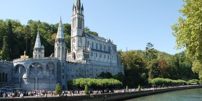 Basílica de Lourdes a orillas del río. El edificio del siglo XX tiene torres altas y muchos peregrinos en las orillas.