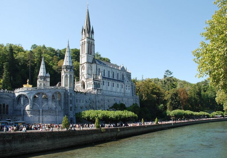 Basílica de Lourdes a orillas del río. El edificio del siglo XX tiene torres altas y muchos peregrinos en las orillas.