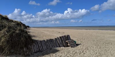 Una playa mayoritariamente arenosa de Utah con una antigua valla de madera y vistas al océano y a las nubes