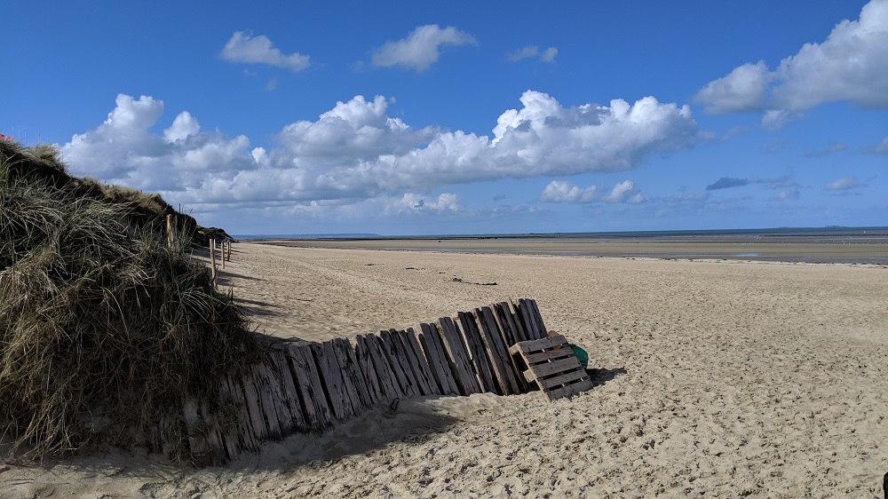 Una playa mayoritariamente arenosa de Utah con una antigua valla de madera y vistas al océano y a las nubes