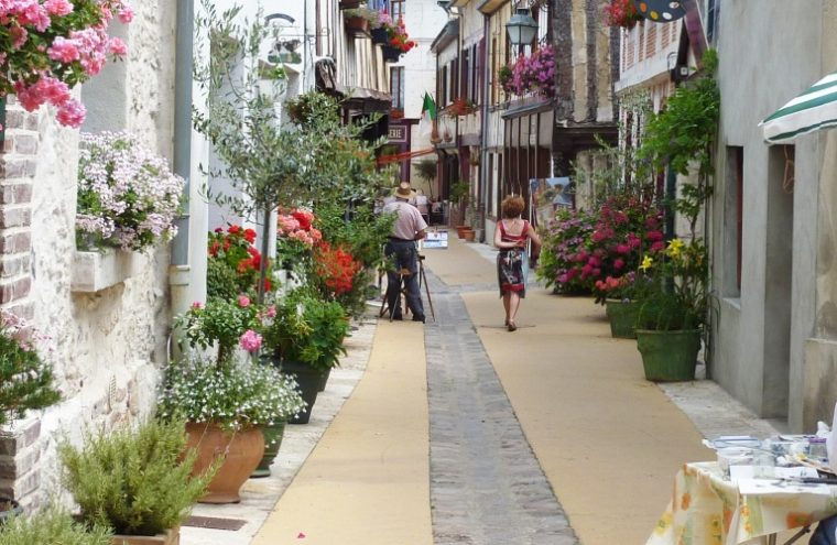 La Bouille Normandy con una estrecha calle peatonal flanqueada por antiguas casas de madera y piedra, macetas y arbustos y dos