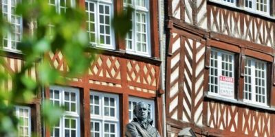 Dos plantas superiores de casas con entramado de madera en Rennes. De color rojo y blanco y marrón y blanco con un árbol al frente y una estatua