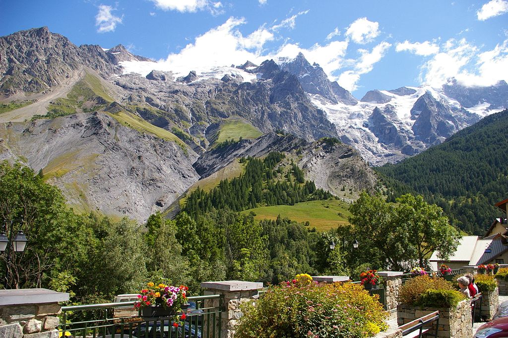 Altas montañas cubiertas de nieve en el fondo en verano, colinas más pequeñas y antiguas casas de piedra frente a La Grave. La montaña La Meije es la imagen de fondo principal.