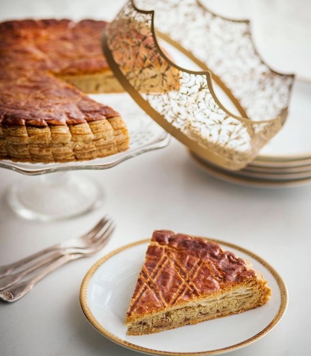 Ladurée galette des rois que muestra un pastel en un soporte con una pieza recortada en un elegante plato con una delicada corona en el costado