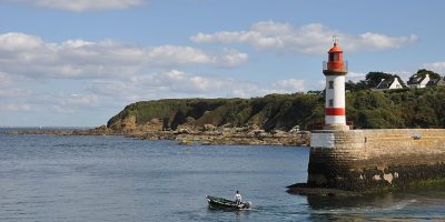 Port Tudy en Ile de Groix Islas Británicas desde el puerto mirando con un pequeño bote cerca del embarcadero con un pequeño faro rojo y blanco mirando el promontorio que pasa por el fondo