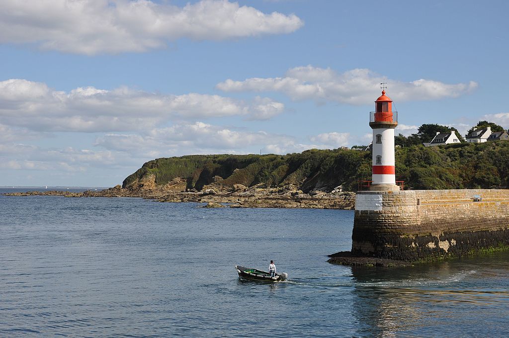 Port Tudy en Ile de Groix Islas Británicas desde el puerto mirando con un pequeño bote cerca del embarcadero con un pequeño faro rojo y blanco mirando el promontorio que pasa por el fondo