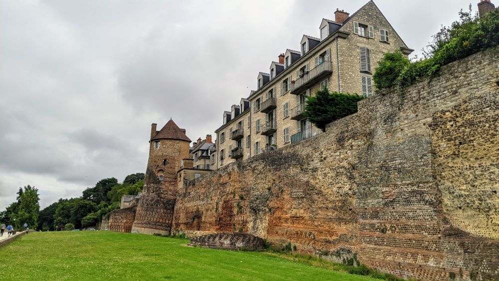 Una vista larga de la muralla romana y luego de la ciudad medieval de Le Mans construida arriba con casas antiguas y torres en la distancia