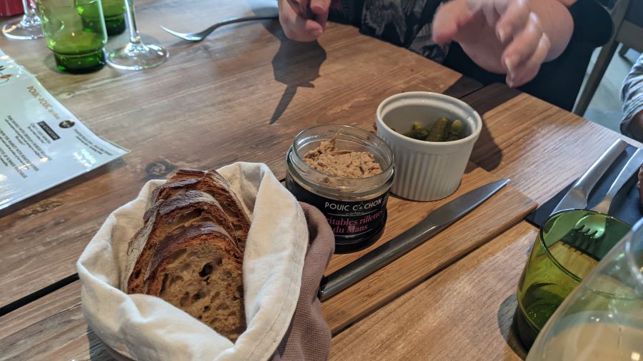 Cesta de pan, rillettes en una olla y pepinillos a bordo en La rotisserie Le Mans