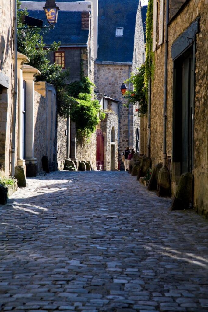 Una estrecha calle adoquinada en Le Mans medieval a la luz del sol que muestra antiguas casas de piedra cubiertas de vegetación