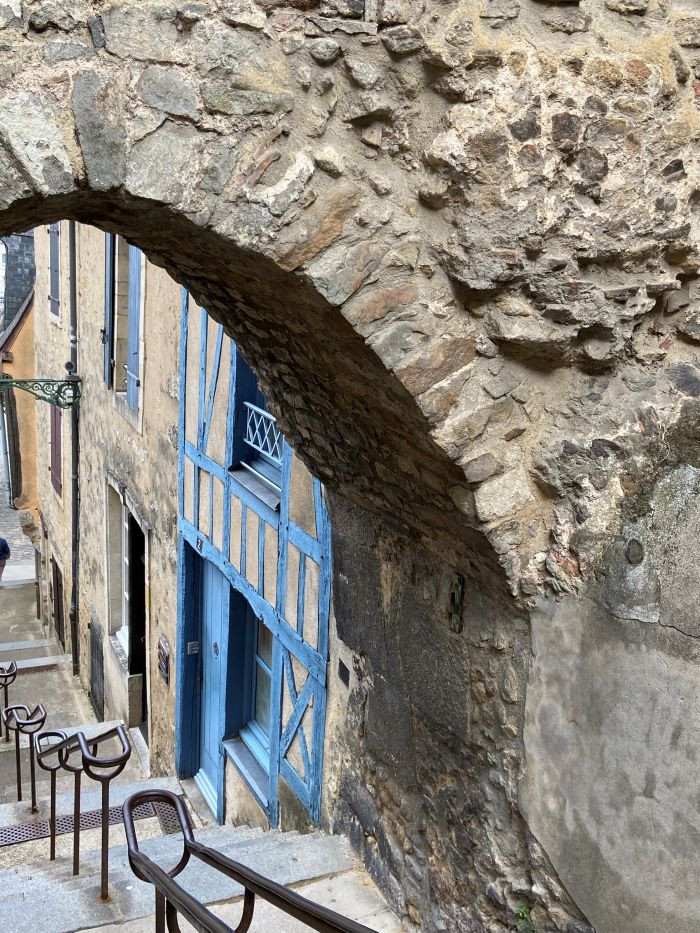 Old Le Mans mirando hacia abajo a través de un arco de piedra en escalones empinados con casas antiguas hechas de piedra y entramado de madera pintada de azul