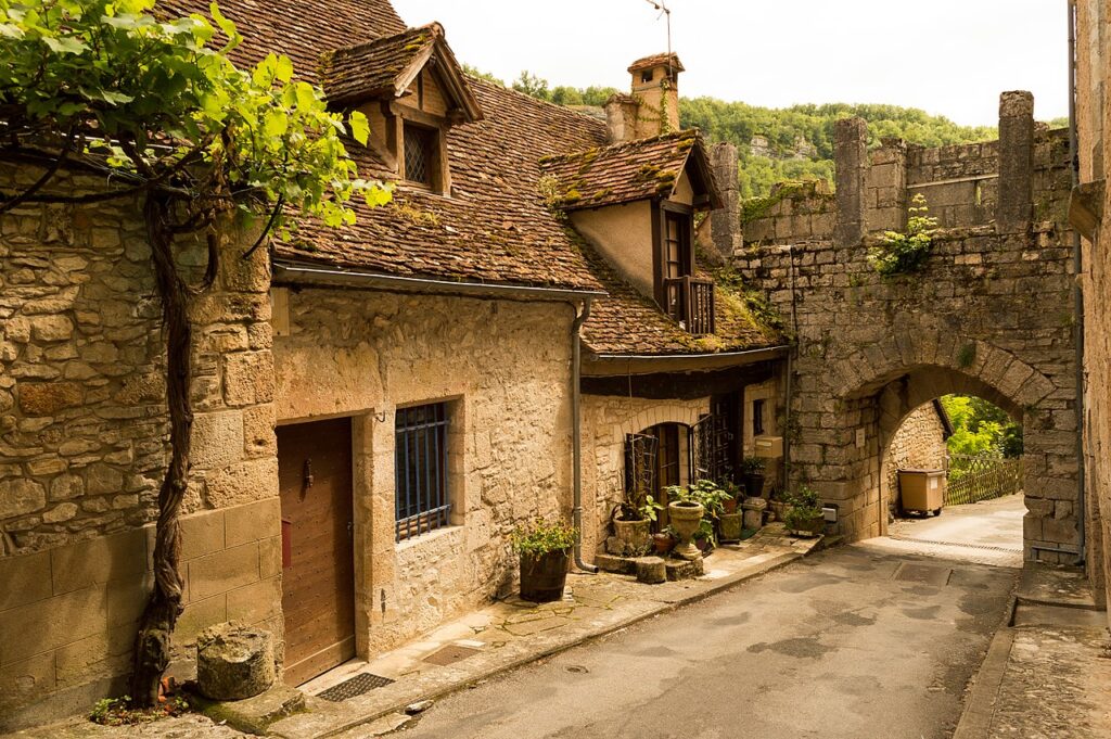 Una pequeña calle montañosa con la casa a la derecha en el camino y la puerta de piedra de Porte Basse en Rocamadour