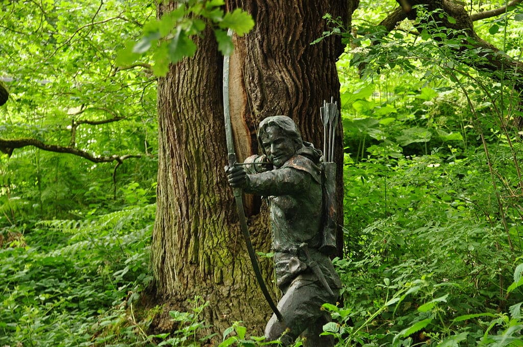 Estatua de Robin Hood en Nottingham Forest que lo muestra apuntando una flecha hacia el espectador con un viejo roble y vegetación detrás