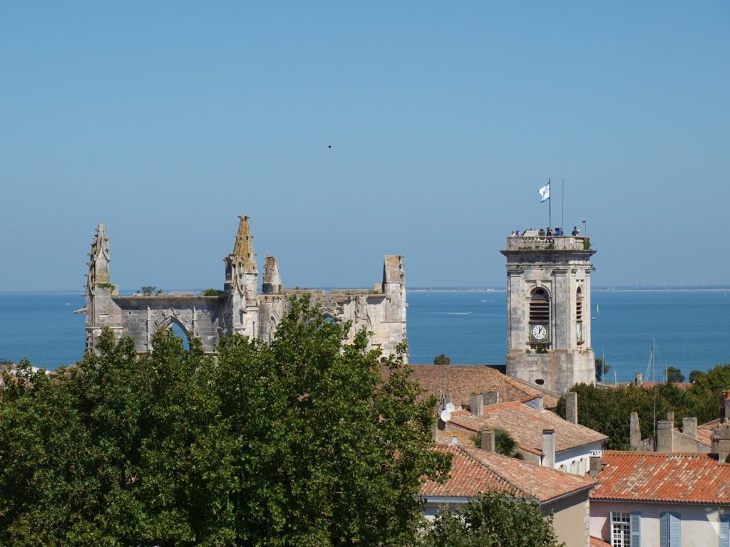 Pueblo de Ile de Ré mirando la torre de la iglesia y las ruinas del castillo desde el nivel de la torre con árboles en primer plano y el mar al fondo