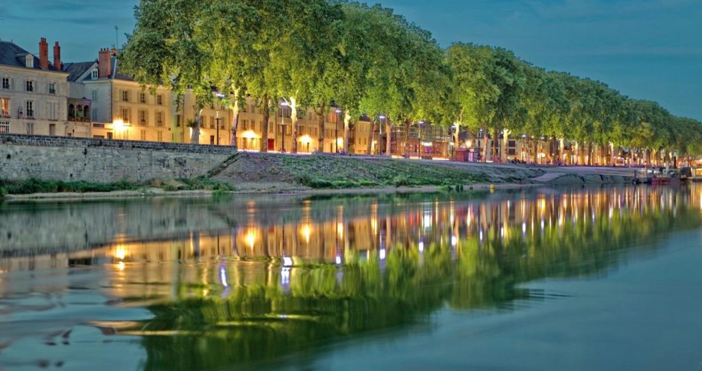 A orillas del río Loira en Orleans por la noche con casas iluminadas a orillas reflejadas en aguas azules y árboles