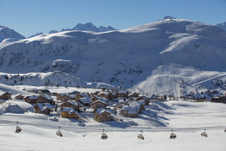 Vista de la estación de esquí de Alpe d'Huez en invierno con teleféricos frente al pueblo y picos nevados detrás