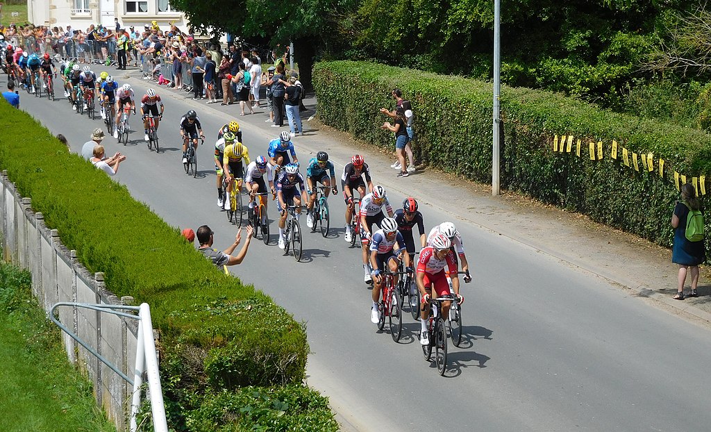 Vista desde arriba de Baugy tour de France 2021 con ciclistas caminando por la carretera en un pequeño pueblo y algunos espectadores
